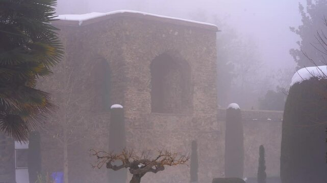 Slow panning shot showing the stone brick construction of Pari Mahal surrounded by shaped landscaped gardens covered in snow hidden by fog on a cold winter evening