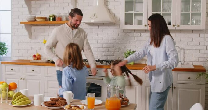 Happy funny young family with little kids eating in modern kitchen together, smiling caring parents have fun, amuse to enjoy weekend meal with small kids, prepare food or breakfast at home