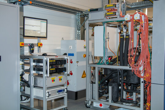 Close-up of industrial testing setup with insulated piping, control units, power supply modules, and structured cable harnesses in a research and monitoring environment