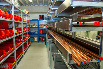 Industrial storage room with organized metal pipe racks and plastic bins filled with various...