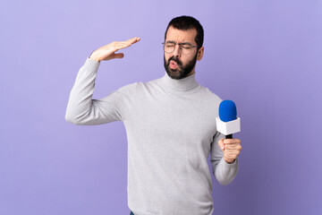 Adult reporter man with beard holding a microphone over isolated purple background with tired and...