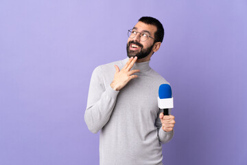 Adult reporter man with beard holding a microphone over isolated purple background looking up while...