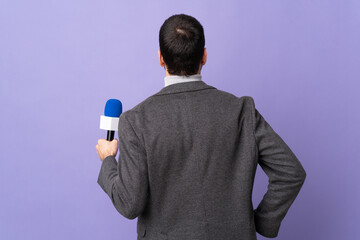 Adult reporter man with beard holding a microphone over isolated purple background in back position