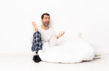 Caucasian man in pajamas sitting on the floor at indoors with surprise facial expression