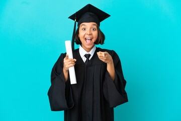 Young university graduate girl over isolated blue background surprised and pointing front