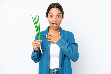 Young hispanic woman holding chive isolated on white background with surprise facial expression