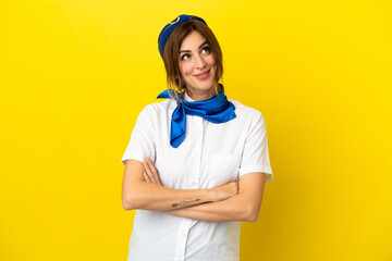 Airplane stewardess woman isolated on yellow background looking up while smiling