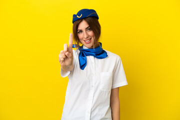 Airplane stewardess woman isolated on yellow background showing and lifting a finger