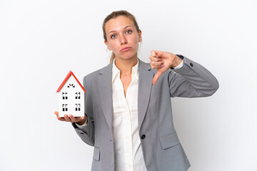 Real estate agent woman holding a toy house isolated on white background showing thumb down with...