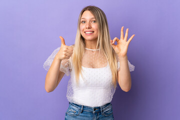Young blonde woman isolated on purple background showing ok sign and thumb up gesture
