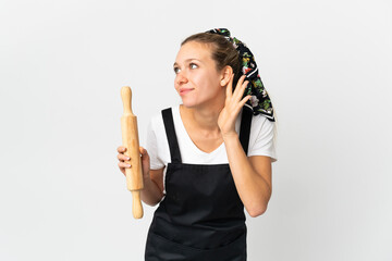 Young woman holding a rolling pin isolated on white background listening to something by putting...