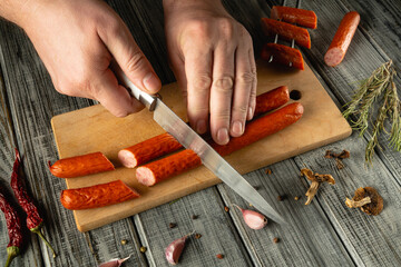 Hands skillfully cut fresh sausage on a wooden board. Fresh herbs and spices are nearby, adding a...