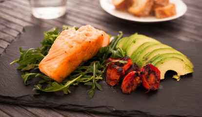 Baked sea trout fillet with fresh vegetables and herbs on black board