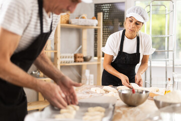 Two bakers place pieces of dough on a baking tray to make croissants