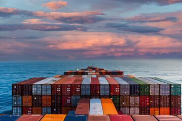 Multicolored shipping containers stacked neatly on the deck of a large cargo ship sail through a...