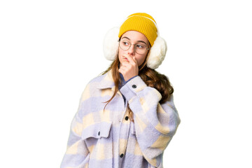 Teenager girl wearing winter muffs over isolated chroma key background having doubts and with...