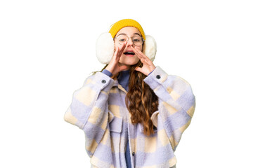 Teenager girl wearing winter muffs over isolated chroma key background shouting and announcing...