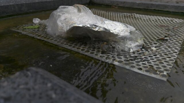 A small stream and a background of dripping rain. A rapid stream of water runs into the sewer with the corresponding sound of the murmur of the stream of water.In the frame there is also a wet plastic