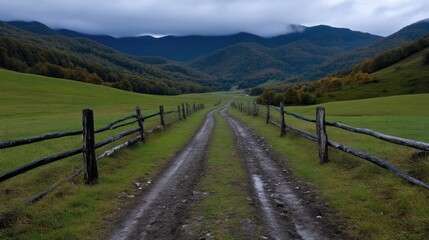 Scenic dirt road winding through a valley, framed by rolling hills and rustic wooden fences.  Misty mountains in the distance
