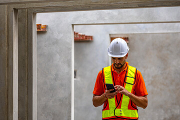 Civil engineer in safety suit is using his smartphone to check the quality of slabs and precast floorboard in production line. Male engineer using mobile application to communicate in a factory.