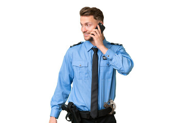 Fototapeta premium Young police man over isolated background keeping a conversation with the mobile phone with someone