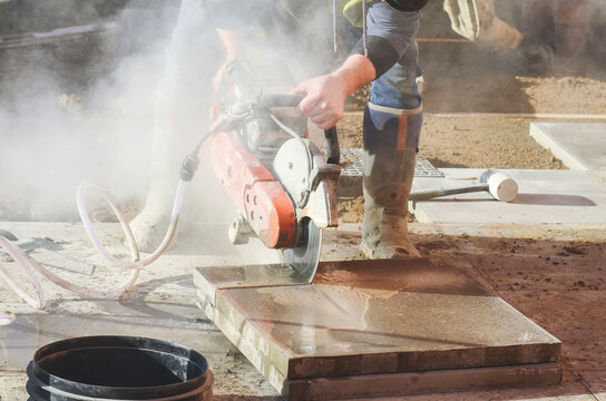 Construction worker using concrete petrol saw to cut paving stones at job site