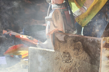 Builder cuts paving slab material on job site using a power tool while dust fills the air
