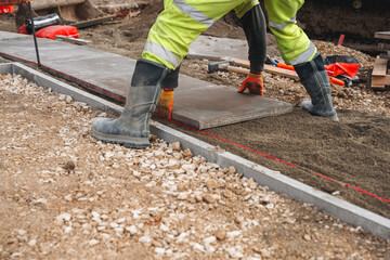 Worker lays concrete paving slab on construction site using tools and equipment for proper...