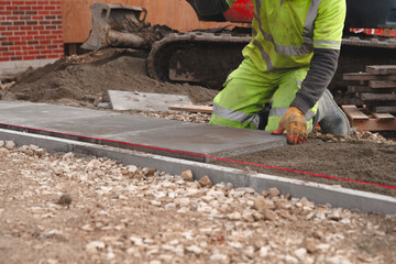 Worker laying concrete paving slabs for sidewalk construction