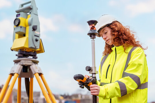 Female Surveying professional adjusts equipment at construction site