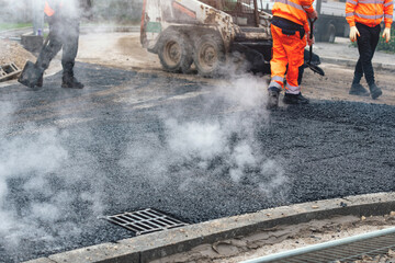Workers lay asphalt on new road under construction, creating  smooth surface while steam rises from the hot material