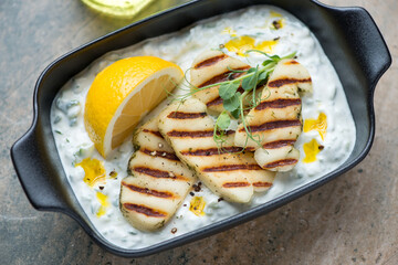 Greek tzatziki or cucumber yogurt sauce with grilled halloumi cheese in a black serving tray, horizontal shot, middle closeup