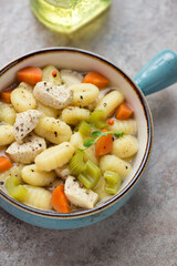 Vegetable soup with chicken fillet and potato gnocchi in a turquoise serving bowl, vertical shot on a brown granite surface, middle close-up