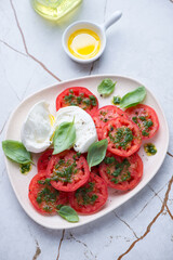 Sliced red tomatoes with torn buffalo mozzarella and basil oil, vertical shot on a white granite background, high angle view