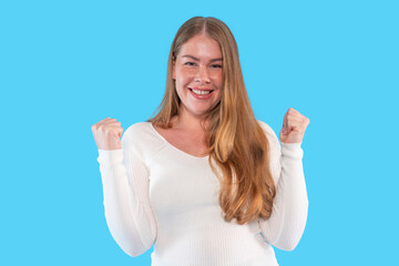 Young woman expresses joy and excitement with raised fists against a bright blue background during...