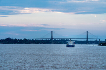 Buque carguero  navegando por el río Paraná, con el puente Rosario-Victoria de fondo, al atardecer