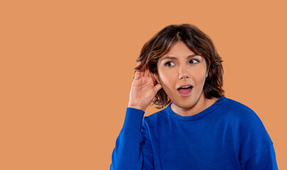 Woman in blue sweater expressing surprise while leaning in to listen attentively against a warm...