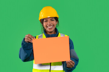 Construction worker smiles while holding orange sign on green background during daytime at a work site in an urban area