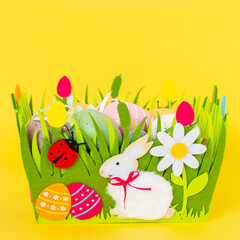 Colorful eggs in decorative felt basket against yellow background. Easter card