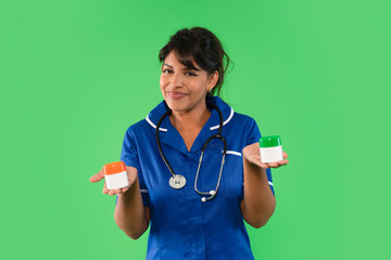 Nurse in blue uniform holding two medicine containers against a green background while smiling confidently