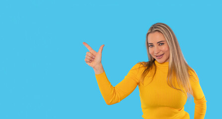 Fototapeta premium Woman in a bright yellow sweater points confidently with smile against a vivid blue background, showcasing a sense of joy and enthusiasm during a cheerful moment
