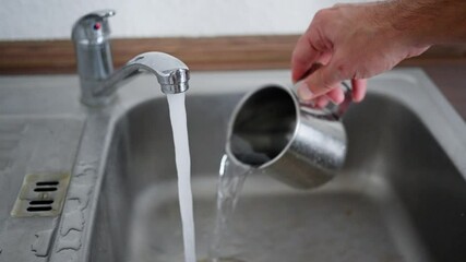 Pouring water from a faucet into a stainless steel cup is a simple daily activity