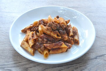 baking penne pasta topping mashed beef meat in sweet and sour sauce on plate    