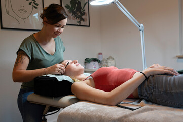 Obraz premium Beauty Close-up of a young woman having her eyelashes microblading brow lash lifting enhanced with an eyelash lift by a beautician in a beauty salon. Shaping eye lash correction