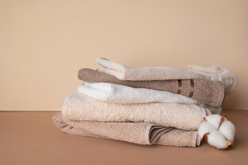 Stack of cotton towels and cotton branch with lush flowers on beige background. Natural bath...