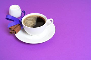 Cup of Black Coffee with Cinnamon and Milk on a Purple Background