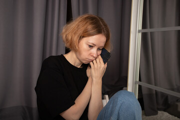 Sad woman with phone at home, lost in thought, facing worry and disappointment in a moment of...