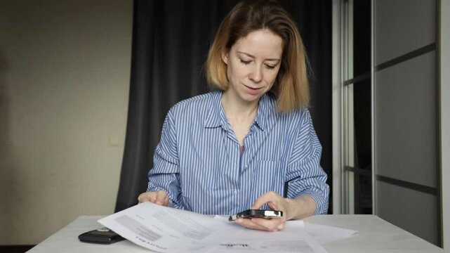 Woman pays utility bills online on smartphone, tracking rising utility costs and energy usage, planning home budget with online banking