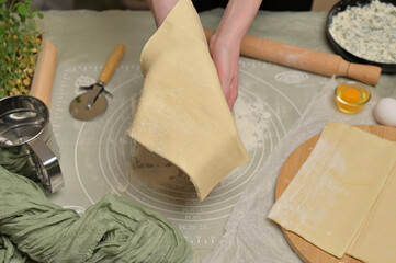 Woman's hands holding a sheet of dough. Rolling pin, cutter, eggs, green towel, microgreens sprouts on kitchen table. Home cooking baking puffs