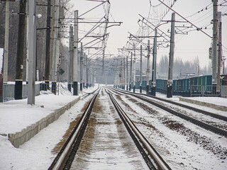 A winter scene at a snowy train station, with a long set of tracks and a distant solitary train...